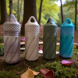 May include: Four cylindrical containers in shades of gray, green, and teal, with textured tops and spiral grooves. The containers are arranged on a bed of green moss with fallen leaves in a forest setting.