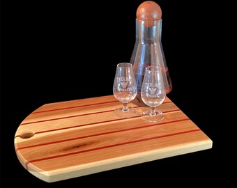 May include: A wooden serving board with red stripes and a hole for pouring. Two clear glasses with the text "Teeling Whiskey" are on the board, along with a glass decanter with a wooden stopper.