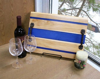 May include: A wooden serving tray with blue stripes and black handles, alongside a bottle of red wine, two wine glasses, and a candle. The tray is rectangular and has a light wood grain.