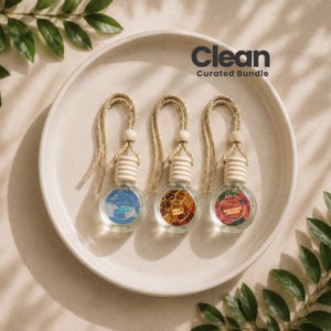 May include: Three small, round glass car air freshener bottles with wooden caps and beige hanging cords, arranged on a circular ceramic plate. Each bottle features a circular label with distinct colours and the text Clean Curated Bundle.