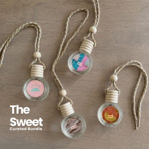 May include: Three clear glass car air freshener bottles with light wood caps and braided rope hangers. Each bottle features a circular label with text: Sugar Stardust, Fairy Floss, Velvet Vanilla, and Peach Candy. The text The Sweet Curated Bundle is visible.