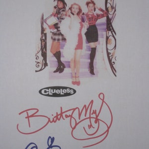 May include: A white background with a black and white image of three girls in school uniforms. The girls are standing on a staircase. The image is from the movie Clueless. The movie title is written in black on a white oval. The image is signed in red ink by Brittany Murphy and in blue ink by Alicia Silverstone.