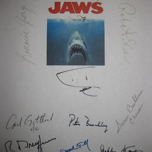 May include: A white sheet of paper with the word "JAWS" in red letters at the top. The paper is signed by several people, including the director, Steven Spielberg, and the actors, Roy Scheider, Robert Shaw, and Richard Dreyfuss.