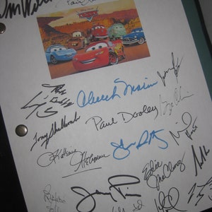 May include: A white sheet of paper with multiple signatures in black and blue ink. A colorful image of the Disney Pixar Cars movie characters is in the center. The signatures are from the cast and crew of the movie.