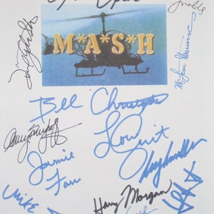 May include: A white sheet of paper with blue and black signatures from the cast of the television show M*A*S*H. The signatures include Alan Alda, Mike Farrell, Jamie Farr, Harry Morgan, Loretta Swit, and others.