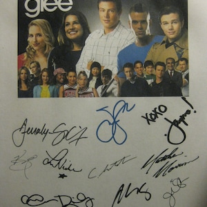 May include: A black and white photo of the cast of Glee, a popular television show. The photo features the actors in character, with the show's title written in white letters on a black background. The photo is signed by several cast members, including Jenna Ushkowitz, Cory Monteith, and Naya Rivera.