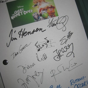 Puede incluir: Una hoja de papel blanca con firmas en tinta negra, algunas en azul. La parte superior de la hoja tiene un póster de la película Disney "The Great Muppet Caper". Las firmas incluyen "Jim Henson" y "Caroll Spinney".