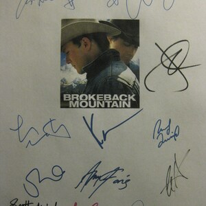 Op de afbeelding: Een witte poster met de titel "Brokeback Mountain" en verschillende handtekeningen in blauwe inkt. De poster toont een zwart-witfoto van twee mannen met cowboyhoeden.