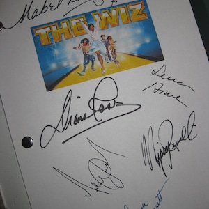 Op de afbeelding: Een wit vel papier met zwarte inktsignatuur van de cast van de musical "The Wiz". De handtekeningen zijn van Mabel King, Sidney Fumet, Diana Ross en Nipsey Russell. De afbeelding bevat ook een foto van de poster van de musical.