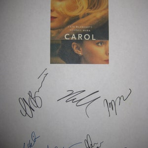 Puede incluir: Un cartel de la película "Carol" con Cate Blanchett y Rooney Mara. El cartel tiene un diseño dividido con los rostros de las actrices. Varias firmas están presentes debajo del cartel sobre un fondo blanco.