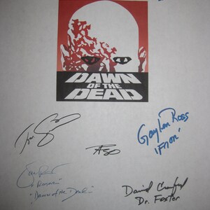 May include: A white sheet of paper with multiple signatures from the cast of the movie "Dawn of the Dead". The signatures are in blue and black ink. The movie poster for "Dawn of the Dead" is in the center of the page. The poster features a zombie with a red and white face and the words "Dawn of the Dead" in black text.