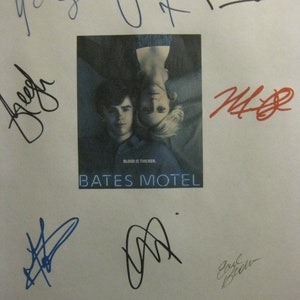 May include: A white sheet of paper with multiple signatures in blue, black, and red ink. The signatures are from the cast of the TV show Bates Motel. The show's title is printed in black text on a blue background. The text "Blood is thicker" is printed in white text on a black background.