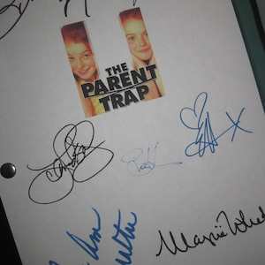 May include: A white sheet of paper with multiple signatures in blue and black ink. The signatures include "Lindsay Lohan", "Natasha Rich", "Mary Kate Olsen", and "Ashley Olsen". The paper also features a movie poster for "The Parent Trap" with a photo of the Olsen twins.
