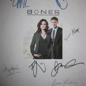Peut inclure: Une feuille de papier blanche avec le mot "BONES" imprimé en noir. Le papier est signé par le casting de la série télévisée "Bones", dont Emily Deschanel, David Boreanaz, Michaela Conlin, T.J. Thyne, Tamara Taylor et Eric Millegan.