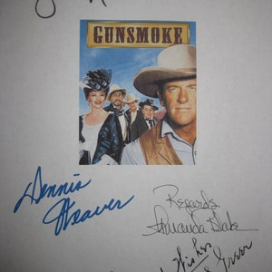 May include: A vintage "Gunsmoke" poster featuring a cowboy with a hat, and other actors. The poster is signed by several people in blue and black ink. The title "Gunsmoke" is in gold letters.
