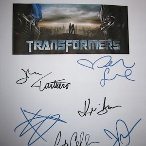 May include: A white poster with the title "Transformers" printed in black. The poster features a movie still of two robots in a city. The poster is signed by five people in blue and black ink.
