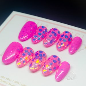 May include: Set of pink press-on nails with iridescent blue and yellow glitter hearts. The nails are in a variety of shapes and sizes.