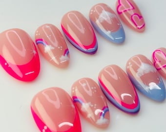 Puede incluir: Un conjunto de uñas postizas ovaladas con varios diseños. Algunas uñas presentan una punta francesa rosa brillante, mientras que otras tienen una base nude con acentos rosas y morados, nubes, arcoíris y corazones.