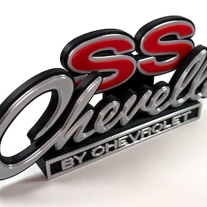Peut inclure: Un emblème Chevrolet SS argenté et rouge avec le texte "BY CHEVROLET" en dessous.