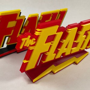 May include: Two 3D printed "The Flash" logos, one red and yellow and the other black and yellow, with a red and yellow lightning bolt base.