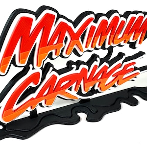 May include: A 3D-printed sign with the words "MAXIMUM CARNAGE" in a stylized font. The text is in red, orange, and white, with a black outline. The sign has a black base and is likely a decorative item.