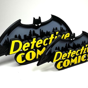 May include: Two black and yellow 3D printed signs with a Batman silhouette and the text "Detective Comics".