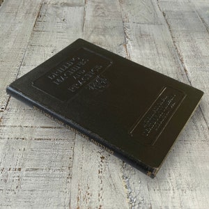 May include: A black leather-bound book titled "Drilling Machines and Practice" with the words "Drilling Machines and Practice" embossed on the spine and "Phillips Machines and Practice" embossed on the front cover.