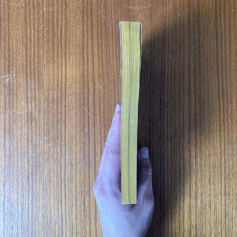 Puede incluir: Un libro con bordes amarillos sostenido por una mano, visto de lado. Las p&aacute;ginas del libro son visibles, y la portada no lo es. El libro est&aacute; sobre un fondo de madera.