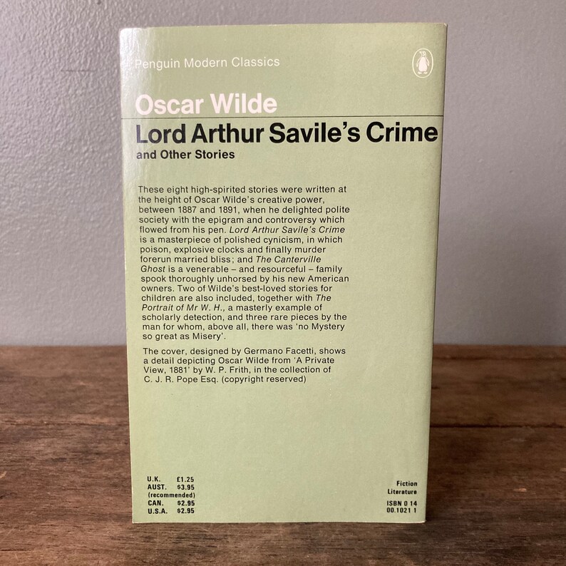 May include: A Penguin Modern Classics paperback book cover featuring a portrait of Oscar Wilde, the author of "Lord Arthur Savile's Crime and Other Stories". The cover is designed by Germano Facetti and features a detail depicting Oscar Wilde from 'A Private View, 1881' by W. P. Frith.