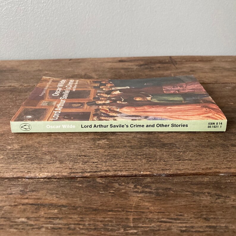 May include: A green paperback book with a picture of a group of people in a room. The book is titled "Lord Arthur Savile's Crime and Other Stories" by Oscar Wilde. The book's ISBN is 0 14 00.1021 1.