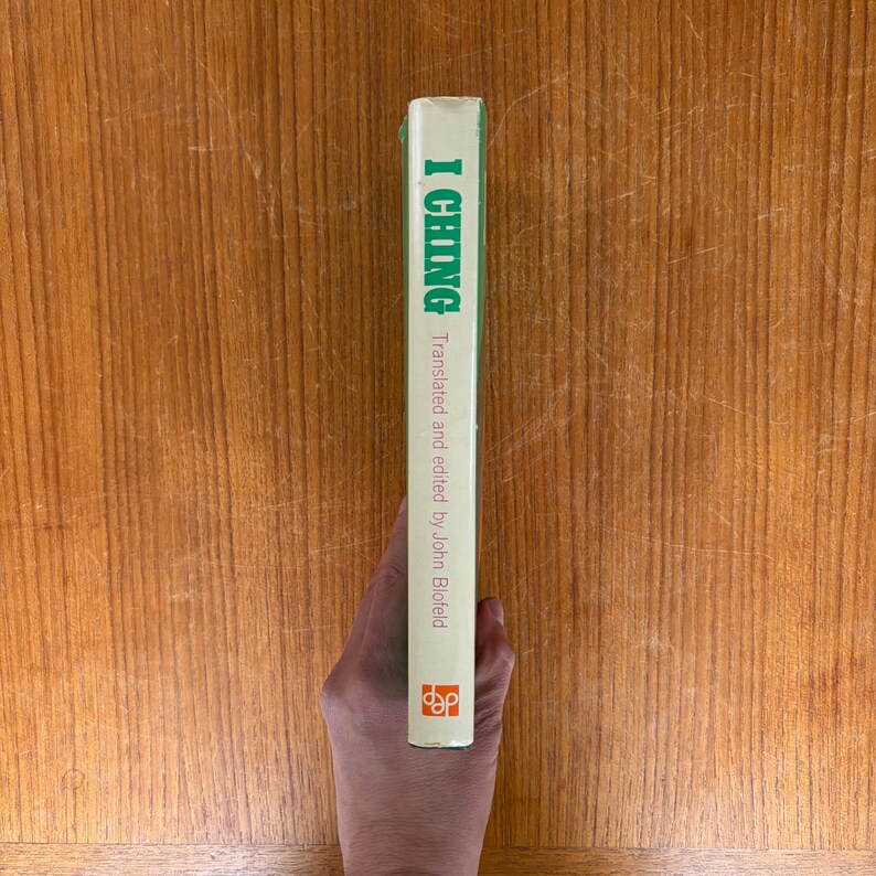 May include: A book spine with the title "I Ching" in green lettering. The text "Translated and edited by John Blofeld" is below the title. The spine is white with a green top and a logo at the bottom.