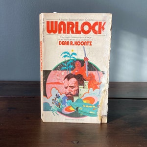 May include: A vintage paperback book cover with a colorful illustration of a man with a beard and a spaceship. The book title is "WARLOCK" and the author is "DEAN R. KOONTZ".