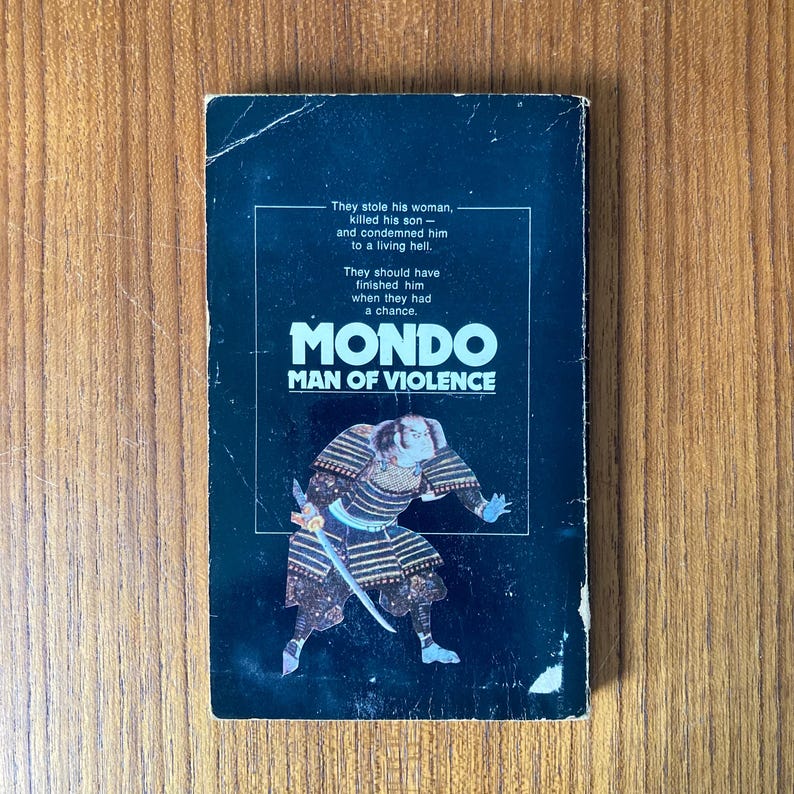 Puede incluir: Portada de libro de bolsillo vintage con el t&iacute;tulo "MONDO MAN OF VIOLENCE". La portada presenta una ilustraci&oacute;n de un guerrero samur&aacute;i con armadura tradicional, sosteniendo una espada. El fondo es azul oscuro con texto blanco.