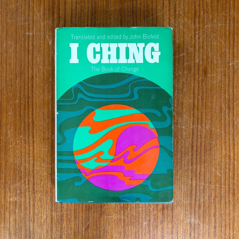 May include: A vintage book titled "I Ching The Book of Change" with a green cover. The cover features a colorful design with a large orange, purple, and teal circular graphic. The book's title and author are in white text.