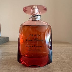 Può includere: Un flacone di profumo in vetro con tappo rosa e liquido color ambra. L'etichetta frontale riporta la scritta Shiseido Ever Bloom Ginza Flower, con il testo Tester - not for sale stampato sotto. Il flacone ha una base larga e un collo argentato.