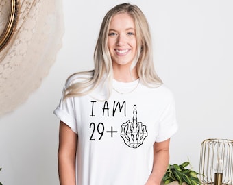 May include: White t-shirt with the text "I AM 29+ " and a skeleton hand giving the middle finger.