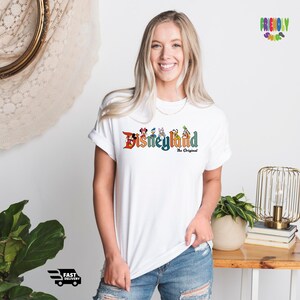 Puede incluir: Camiseta blanca con un gr&aacute;fico colorido del logotipo de Disneyland y personajes. El texto dice "Disneyland The Original".