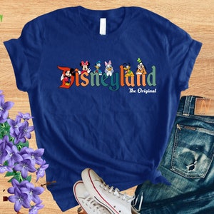 Puede incluir: Una camiseta azul con un gr&aacute;fico colorido de Mickey Mouse, Minnie Mouse, Donald Duck, Goofy, Pluto y un perro de dibujos animados. El gr&aacute;fico dice "Disneyland The Original".