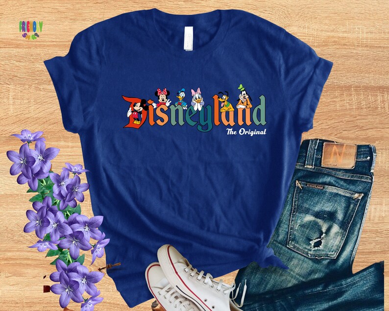 Puede incluir: Una camiseta azul con un gr&aacute;fico colorido de Mickey Mouse, Minnie Mouse, Donald Duck, Goofy, Pluto y un perro de dibujos animados. El gr&aacute;fico dice "Disneyland The Original".