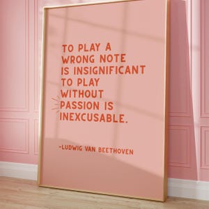 K&ouml;nnte beinhalten: Ein rosa Poster mit goldenem Rahmen, auf dem ein Zitat von Ludwig van Beethoven steht: "Einen falschen Ton zu spielen ist unbedeutend. Ohne Leidenschaft zu spielen ist unverzeihlich."