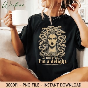 May include: A black t-shirt featuring a graphic illustration of Medusa with snakes for hair, wearing an ornate necklace. Below the illustration, the text reads, "first of all, I'm a delight." The design is rendered in shades of gold and tan.