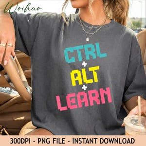 Może przedstawiać: Ciemnoszary t-shirt z krótkim rękawem z pikselowym tekstem w trzech kolorach. Górny wiersz to CTRL w kolorze jasnoniebieskim, środkowy to ALT w kolorze żółtym, a dolny to LEARN w kolorze różowym, z białymi znakami plus pomiędzy nimi.
