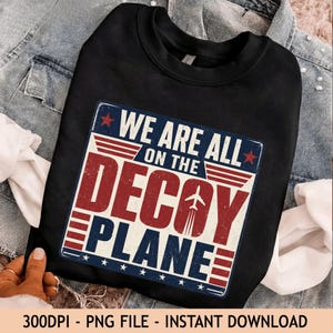 Può includere: Una felpa nera a girocollo con un design grafico che riporta il testo WE ARE ALL ON THE DECAY PLANE. Il design include una piccola icona di aereo, strisce rosse e blu e stelle rosse, il tutto presentato con una texture in stile vintage.