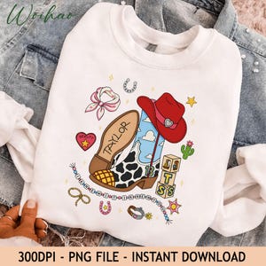 May include: A white crewneck sweatshirt featuring a graphic print of a cowboy boot with a cow print pattern, a red cowboy hat, a pink bandana, a cactus, and wooden blocks. The text "TAYLOR" is on the boot, and "I KNEW IT I KNEW YOU" is printed.