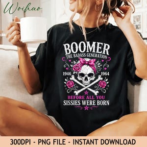 May include: A black t-shirt featuring a graphic of a skull wearing a pink bandana with roses and crossed bones. The text reads BOOMER THE BADASS GENERATION 1946 1964 BEFORE ALL YOU SISSIES WERE BORN. The design includes pink stars and decorative flourishes.