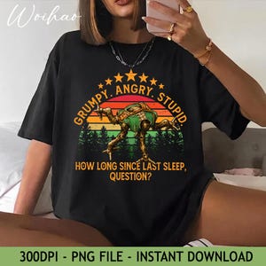 May include: Black t-shirt with a graphic featuring a creature and the text "GRUMPY. ANGRY. STUPID." and "HOW LONG SINCE LAST SLEEP, QUESTION?". The design includes a sunset and forest background.