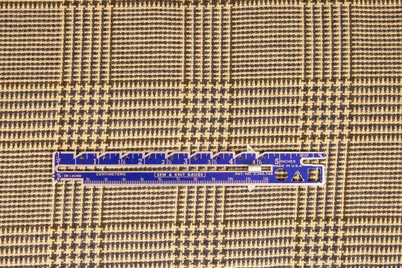 Puede incluir: Un primer plano de una tela de pata de gallo beige y negra con una regla que mide 5 pulgadas. La regla es azul con marcas blancas y el texto "5 inches made in U.S.A."