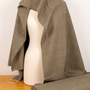 Puede incluir: Tela de cuadros marrones y beige drapeada sobre un maniqu&iacute;. La tela est&aacute; doblada y enrollada sobre una superficie de madera.