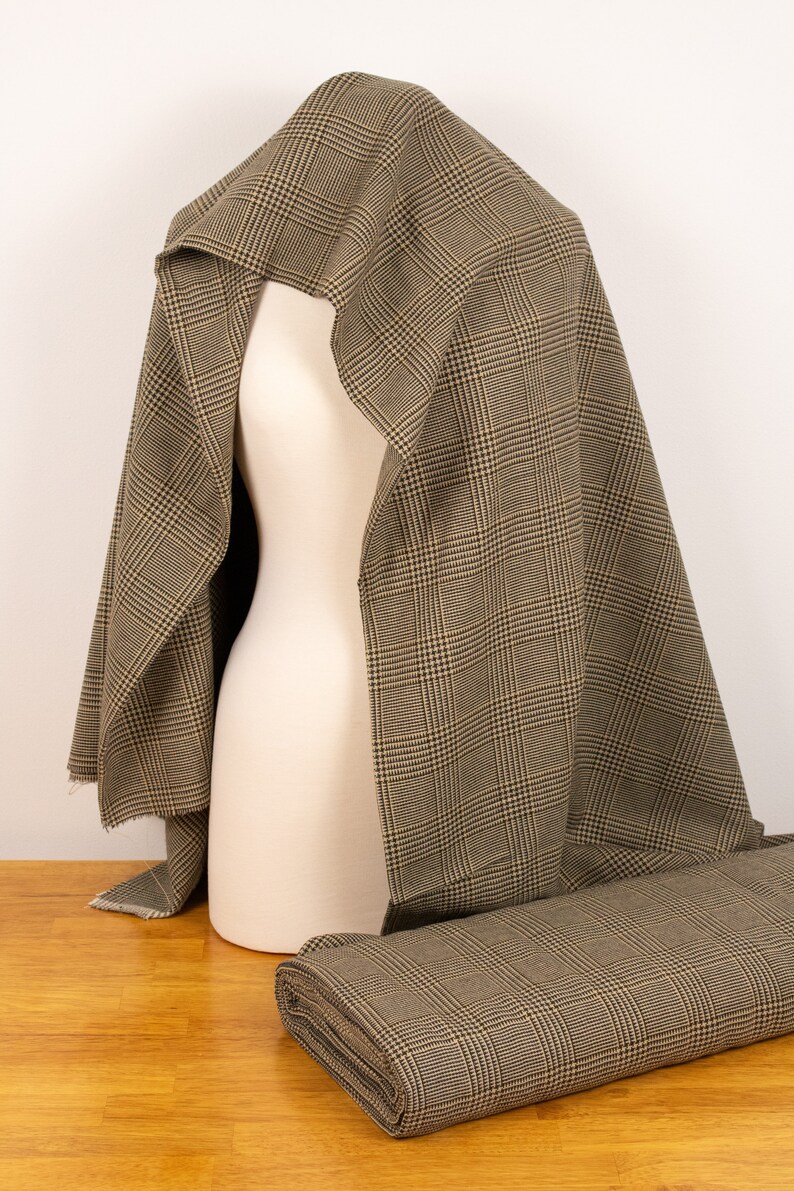 Puede incluir: Tela de cuadros marrones y beige drapeada sobre un maniqu&iacute;. La tela est&aacute; doblada y enrollada sobre una superficie de madera.