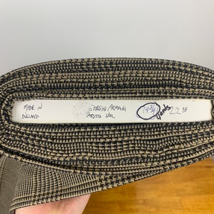 Puede incluir: Primer plano de un rollo de tela con estampado marr&oacute;n y negro con una etiqueta blanca que dice "Made in England" y "Giorgio Armani Worsted Wool" con una nota manuscrita que dice "14 3/4 Yards 22.98".